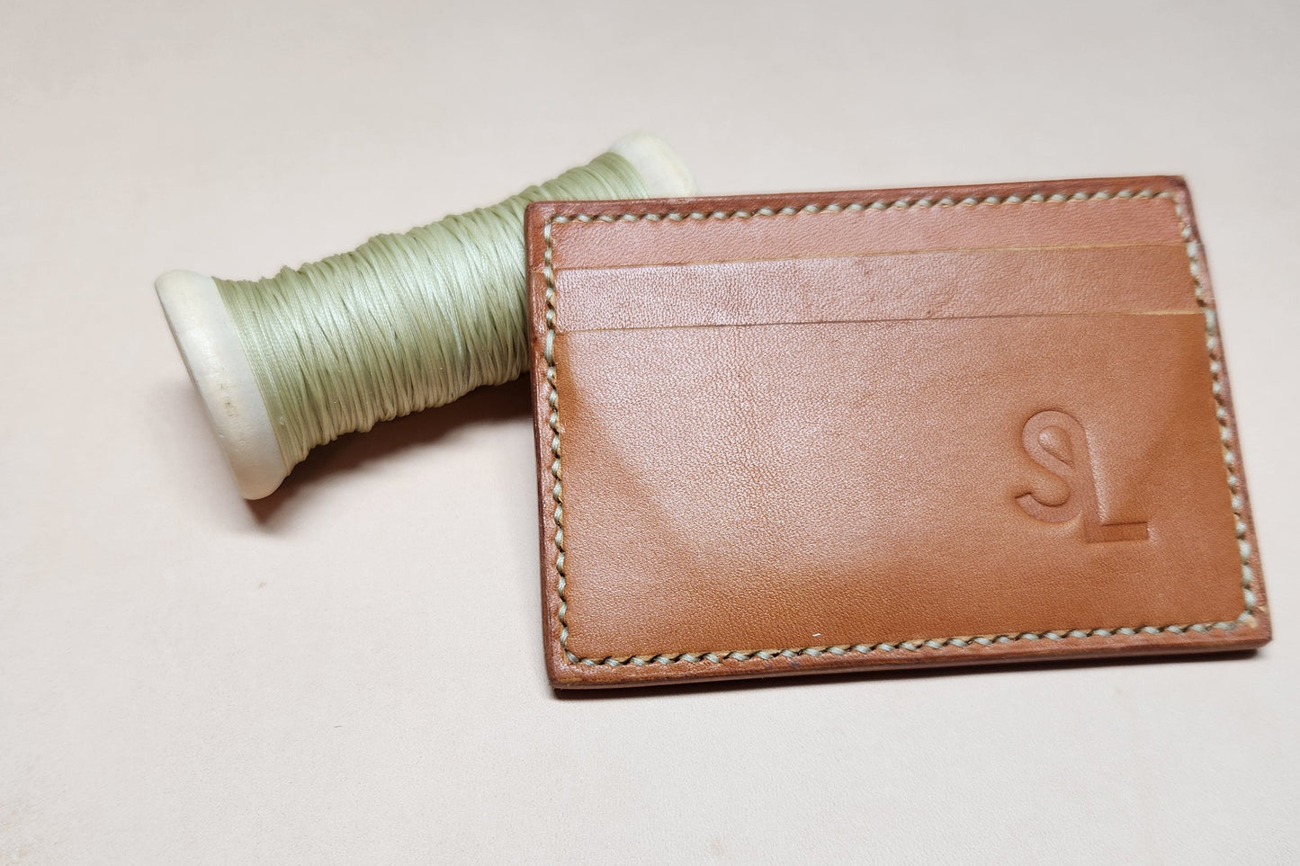 Brown leather wallet with a spool of thread on a light background